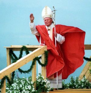 Jan Paweł II w czerwonym ornacie błogosławi prawą dłonią wiernych, w lewej dłoni trzyma srebrny pastorał.